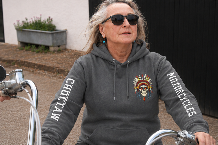Person wearing a gray hoodie with motorcycle design and text, sitting on a motorcycle.