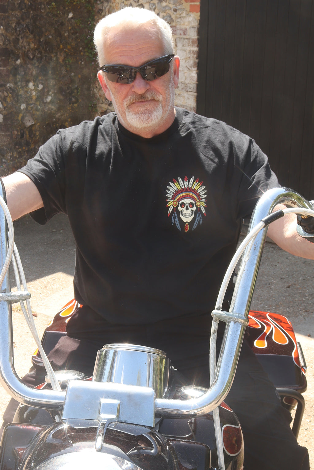 Man wearing sunglasses and a black t-shirt with a skull design, sitting on a motorcycle.