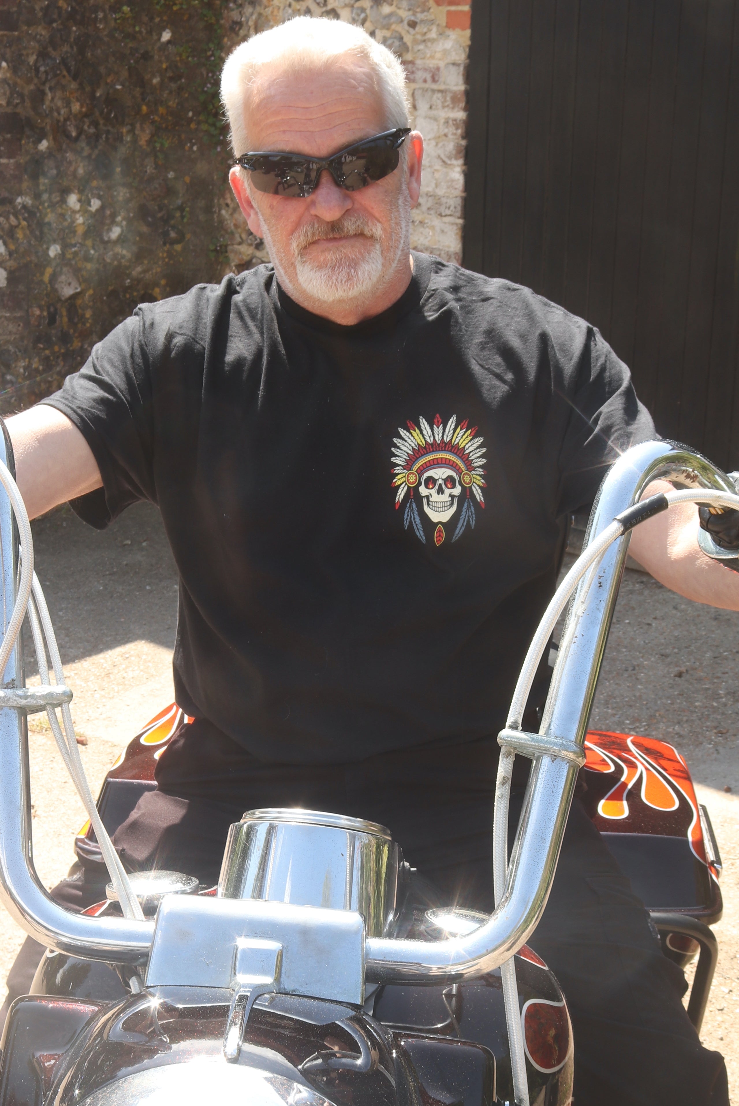 Man wearing sunglasses and a black t-shirt with a skull design, sitting on a motorcycle.