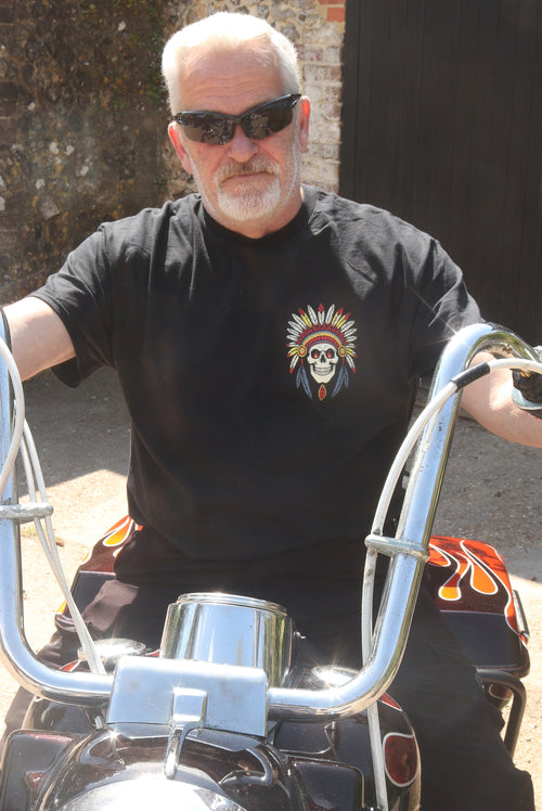 Man wearing sunglasses and a black t-shirt with a skull design, sitting on a motorcycle.