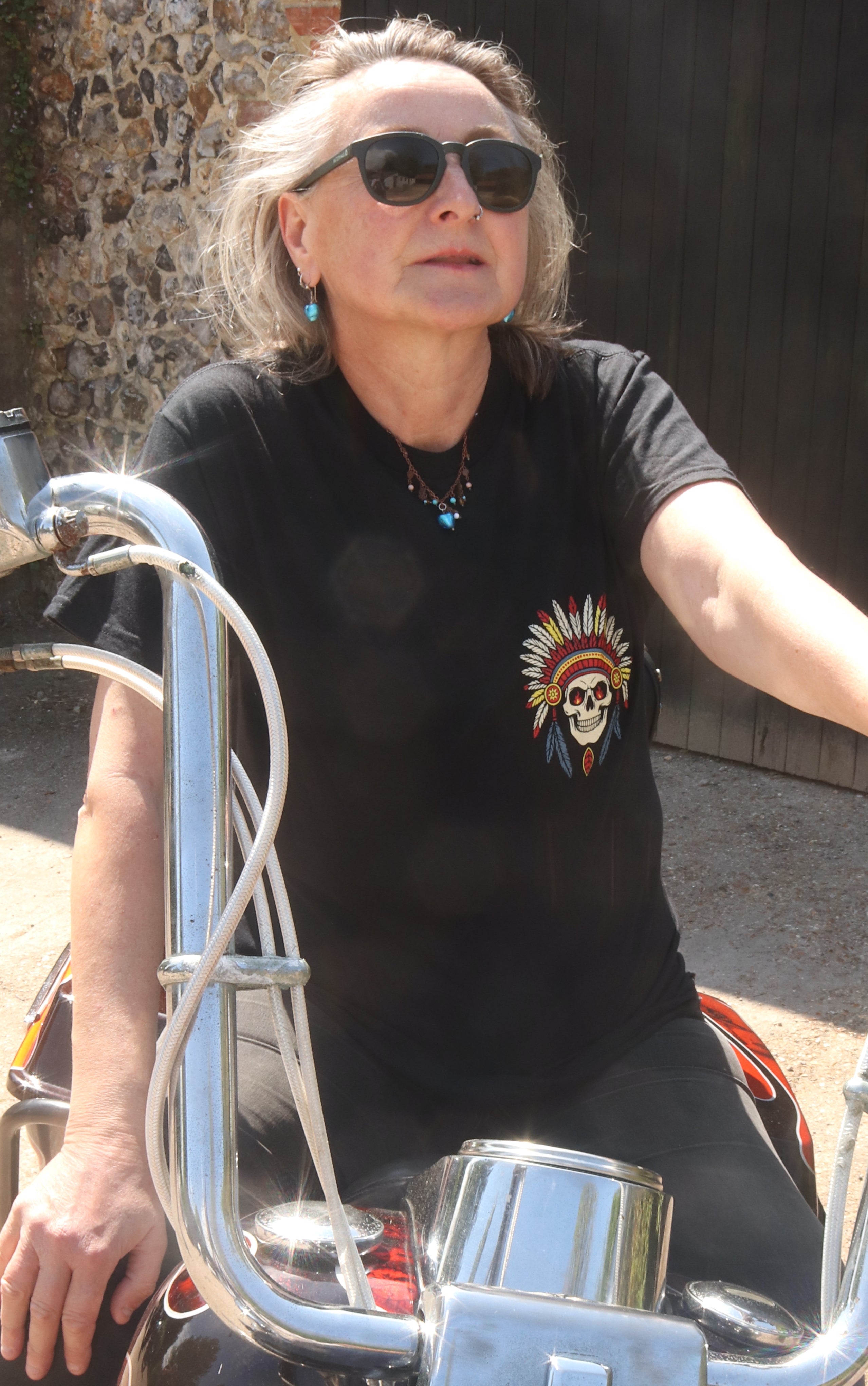 Person wearing sunglasses and a black t-shirt with a skull design, sitting on a motorcycle.