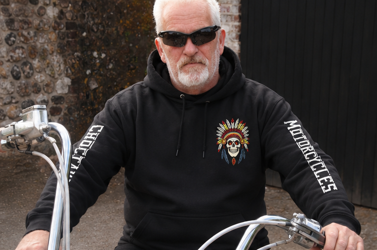 Man wearing a black hoodie with a motorcycle-themed design, sitting on a vintage bike.