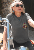 Person wearing sunglasses and a gray t-shirt with a colorful design, sitting on a motorcycle.